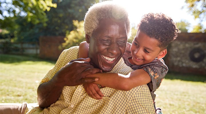 Senior-black-man-sitting-on-grass,-embraced-by-his-grandson